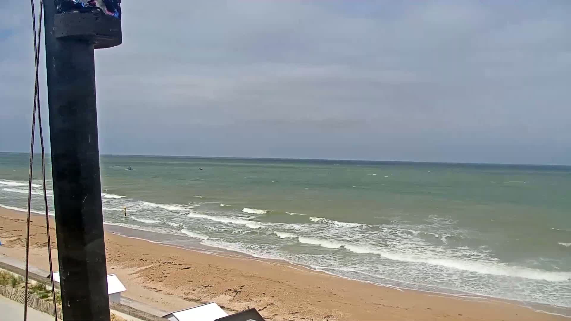 A sandy beach with moderate waves under a partly cloudy sky is visible from behind a dark pole.