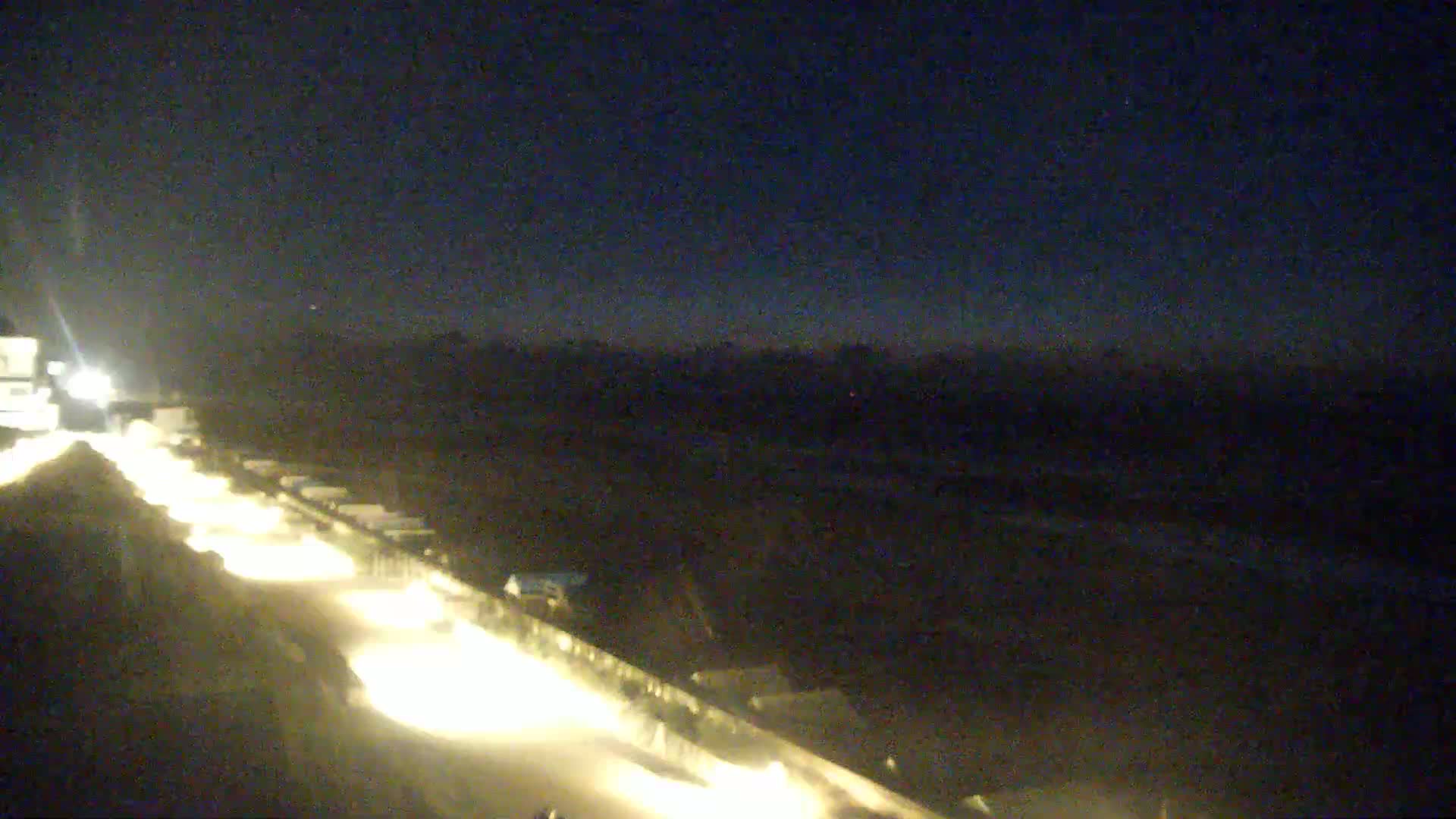 At night, a long line of vehicle headlights illuminates a road next to a dark beach under a clear, dark sky.