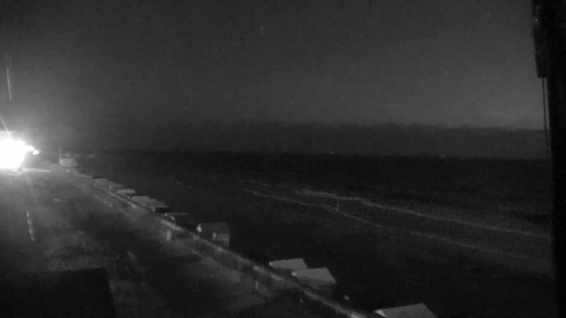 A nighttime, low-light view of a highway with a few vehicles visible in the distance and some structures alongside the road.