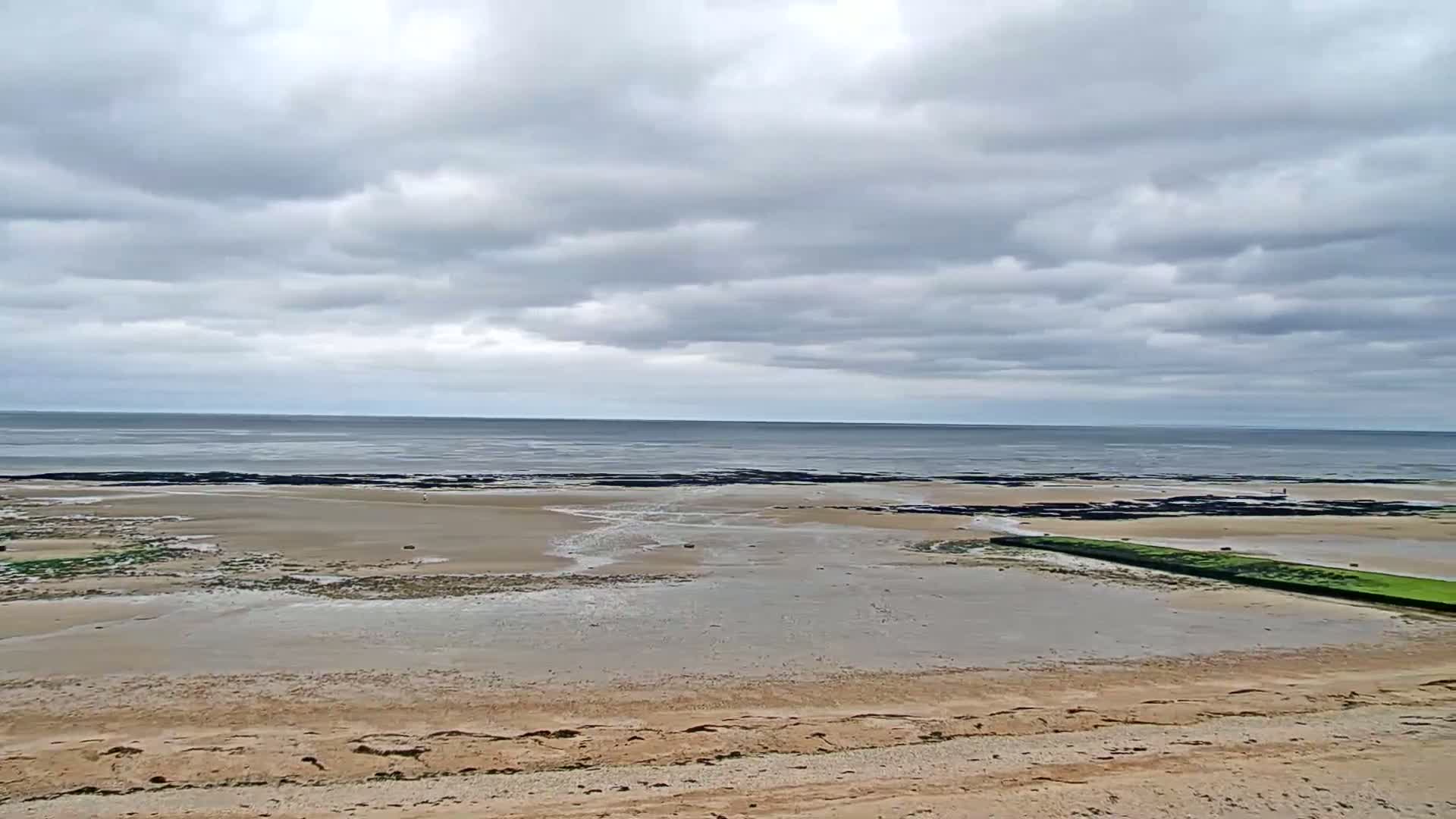 A sandy beach stretches toward a calm sea under a cloudy sky.