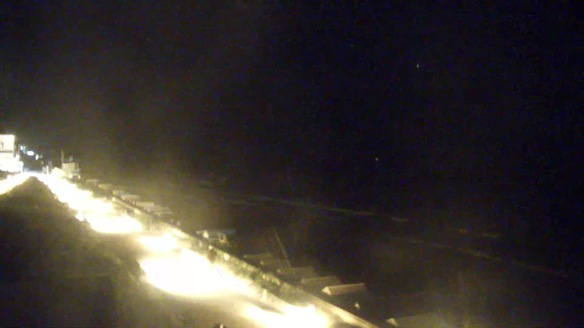 A nighttime, blurry view of a roadway with vehicle headlights visible, possibly near a shoreline.