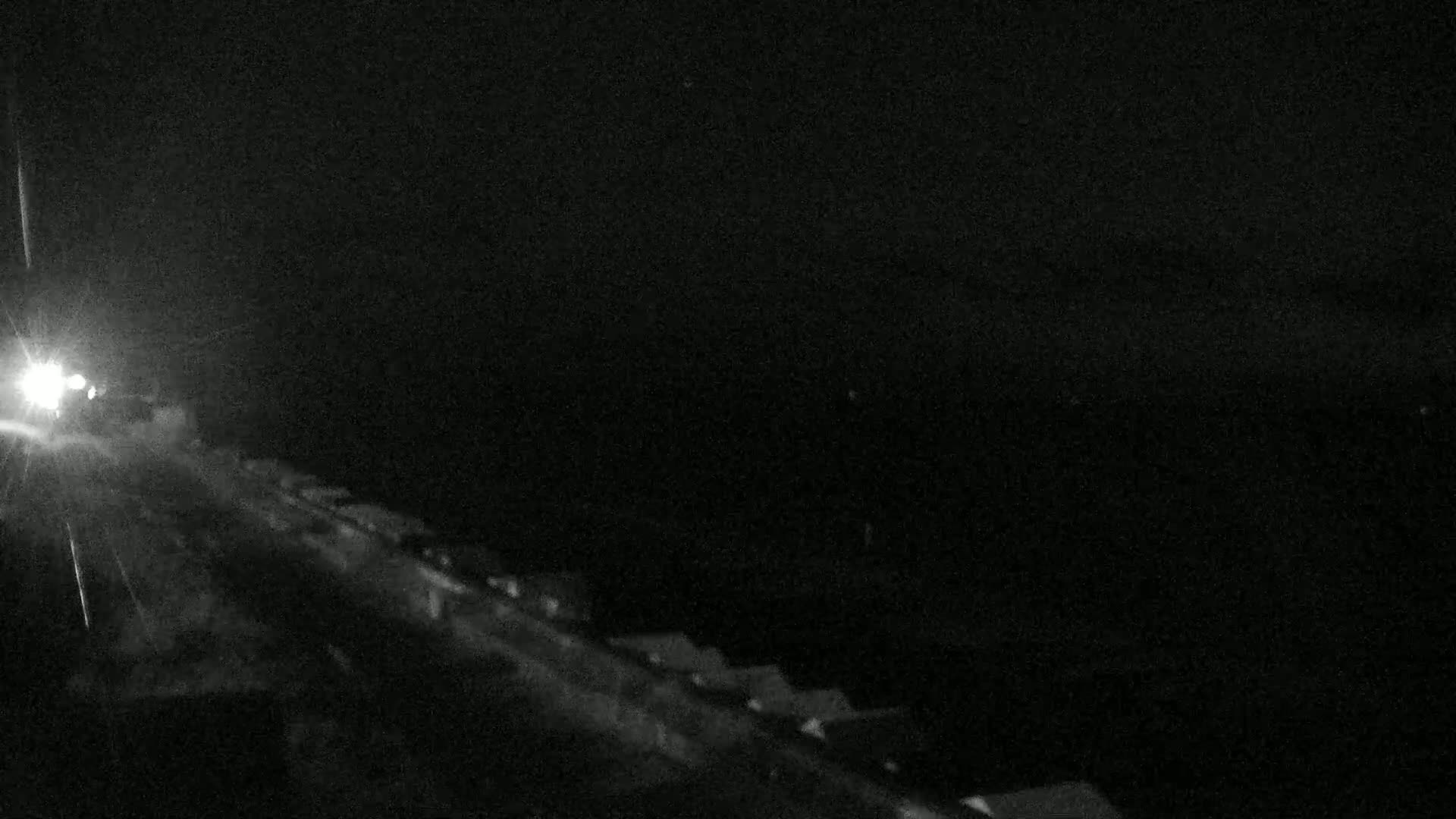 A nighttime, low-light view of a road with a vehicle's headlights visible in the distance.
