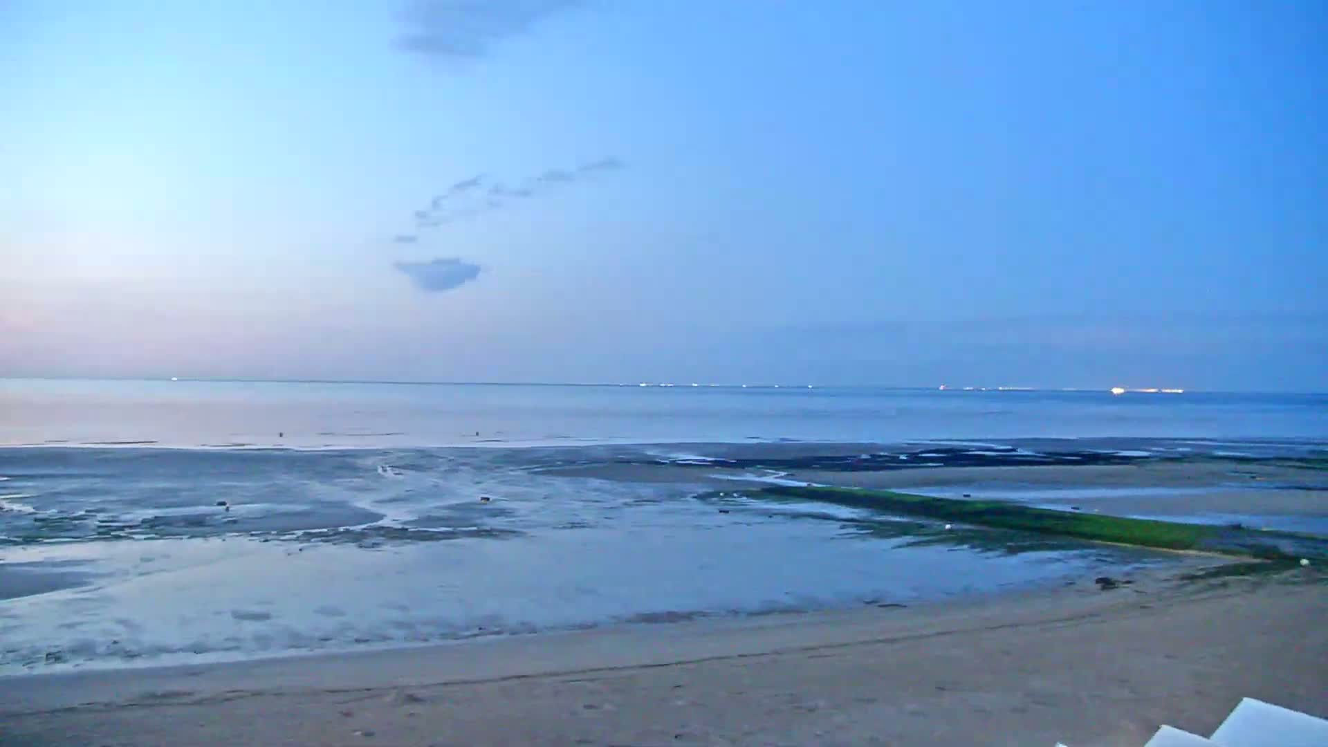 A calm, twilight ocean stretches to the horizon, meeting a wide expanse of exposed, wet sand and mudflats.