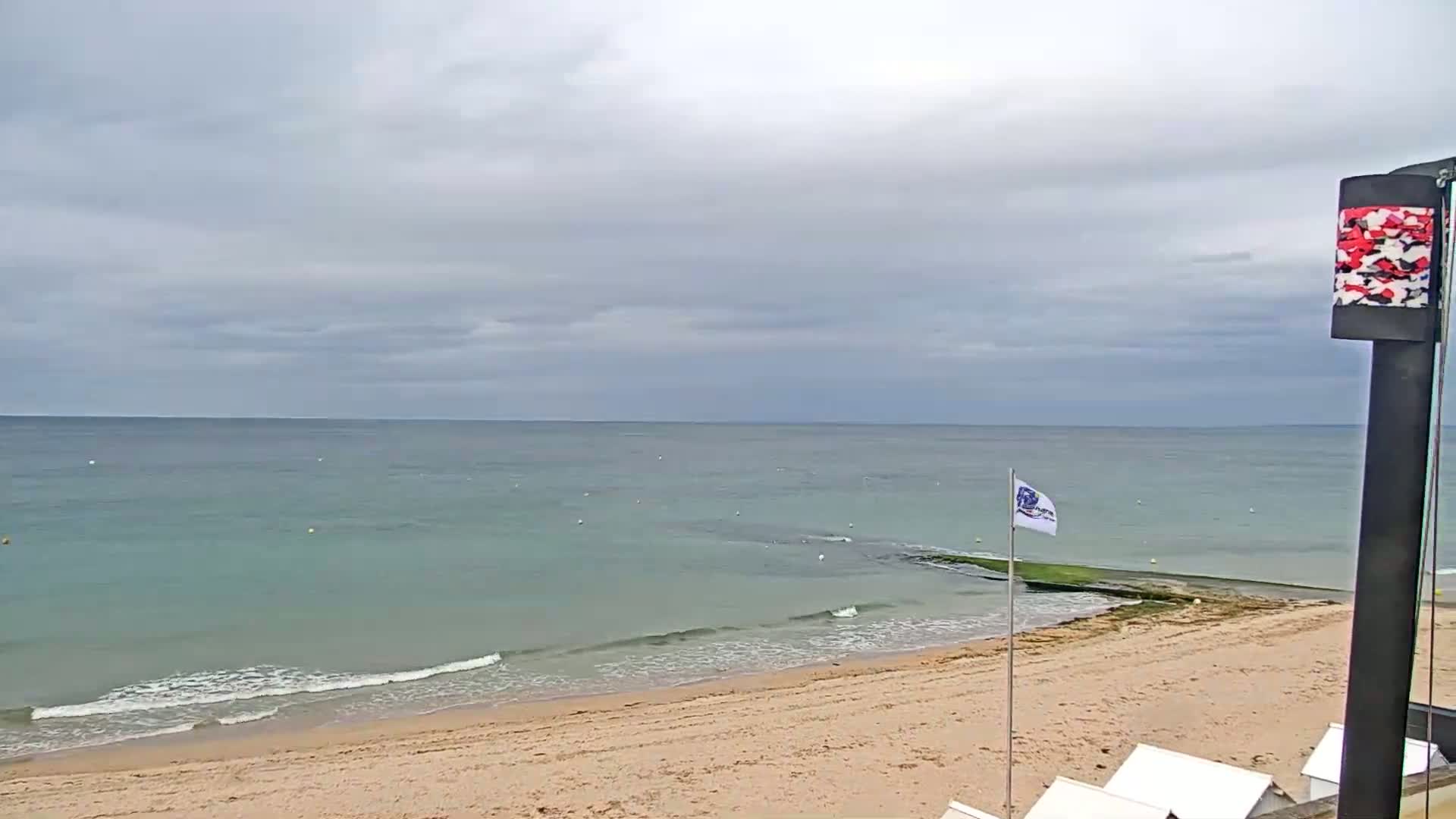 A sandy beach with calm, teal water under a cloudy sky.