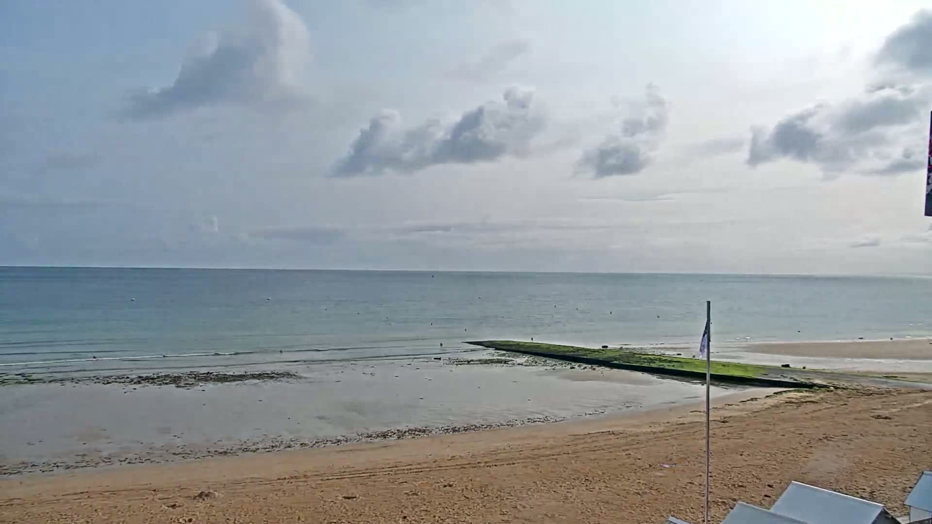 A sandy beach stretches to a calm, blue ocean under a partly cloudy sky.