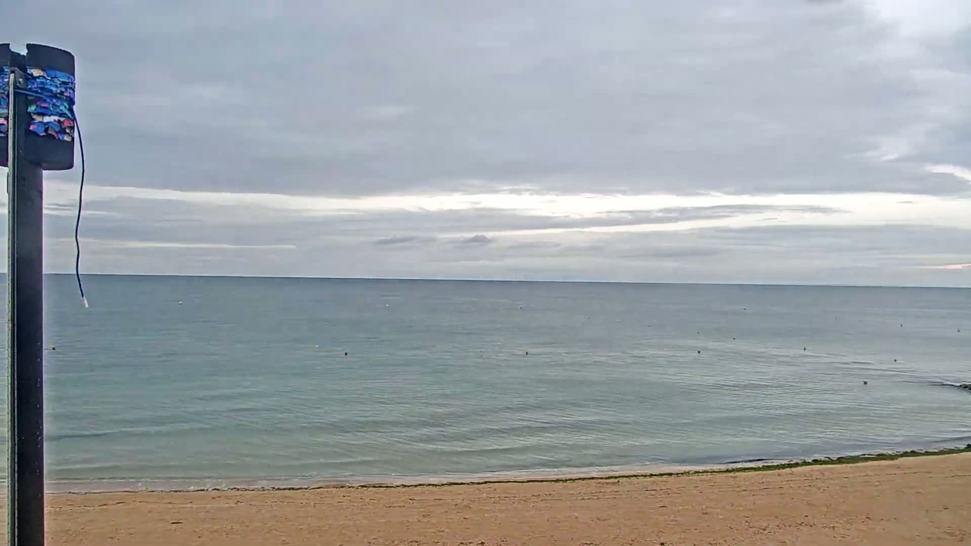 A calm, light-grey ocean meets a sandy beach under an overcast sky.