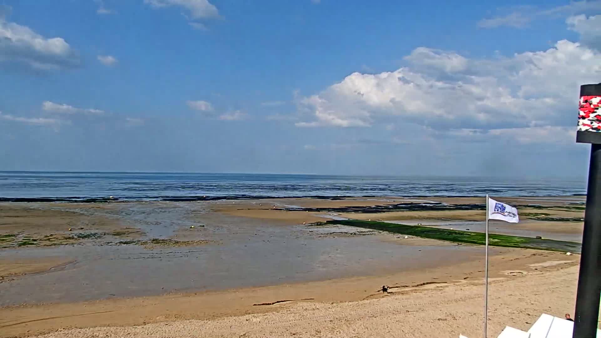 A sandy beach stretches out to a calm sea under a partly cloudy sky.