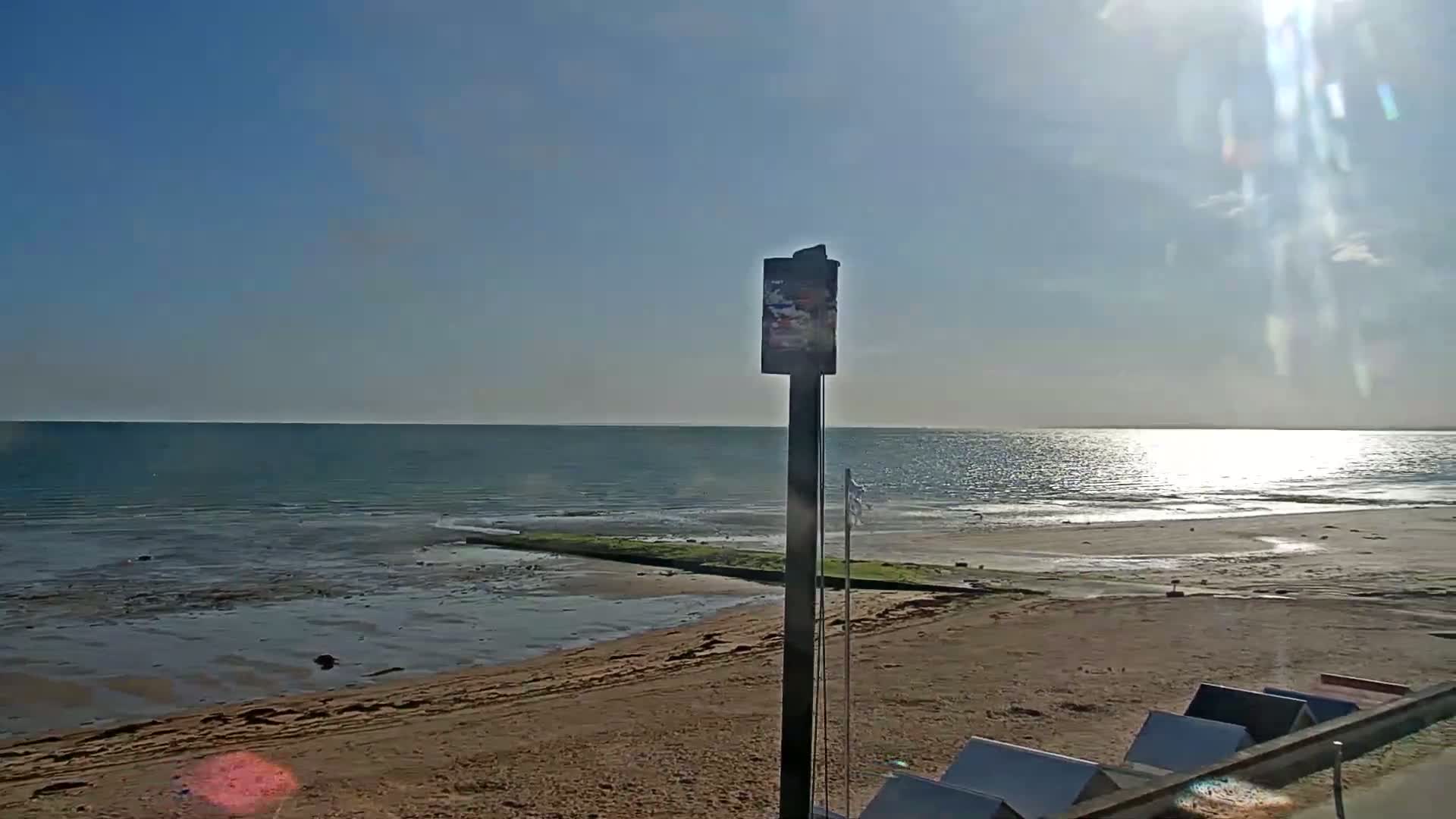 A sandy beach stretches out to a calm, sunlit sea under a clear blue sky.