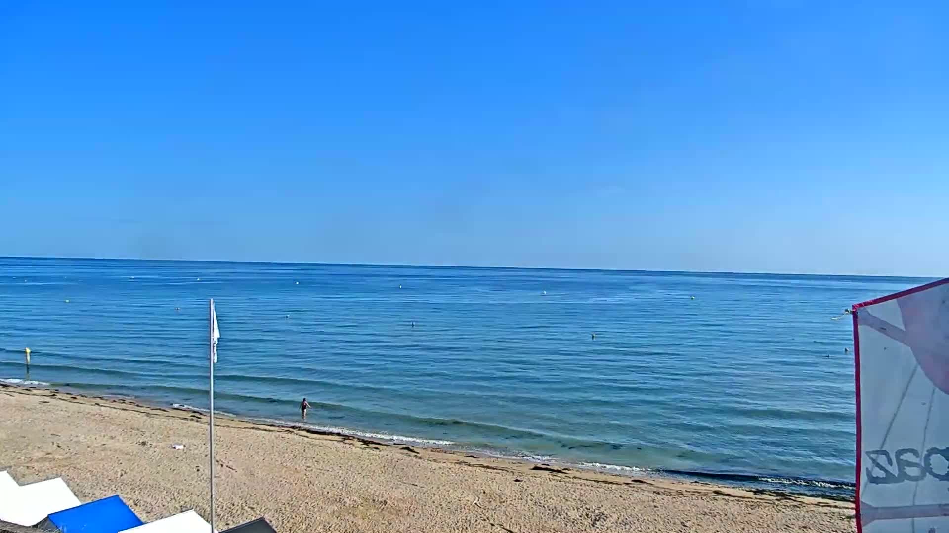 A sandy beach slopes down to a calm, blue ocean under a clear blue sky.