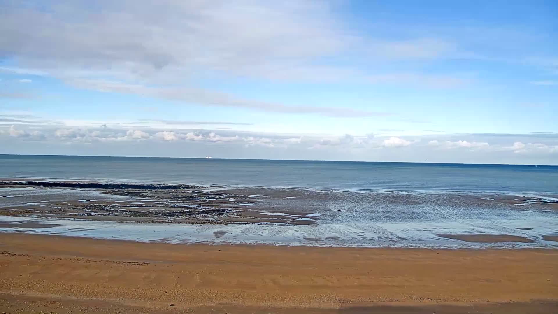 A nighttime beach scene shows a dimly lit boardwalk with several flags and a dark ocean with small waves under a clear sky.