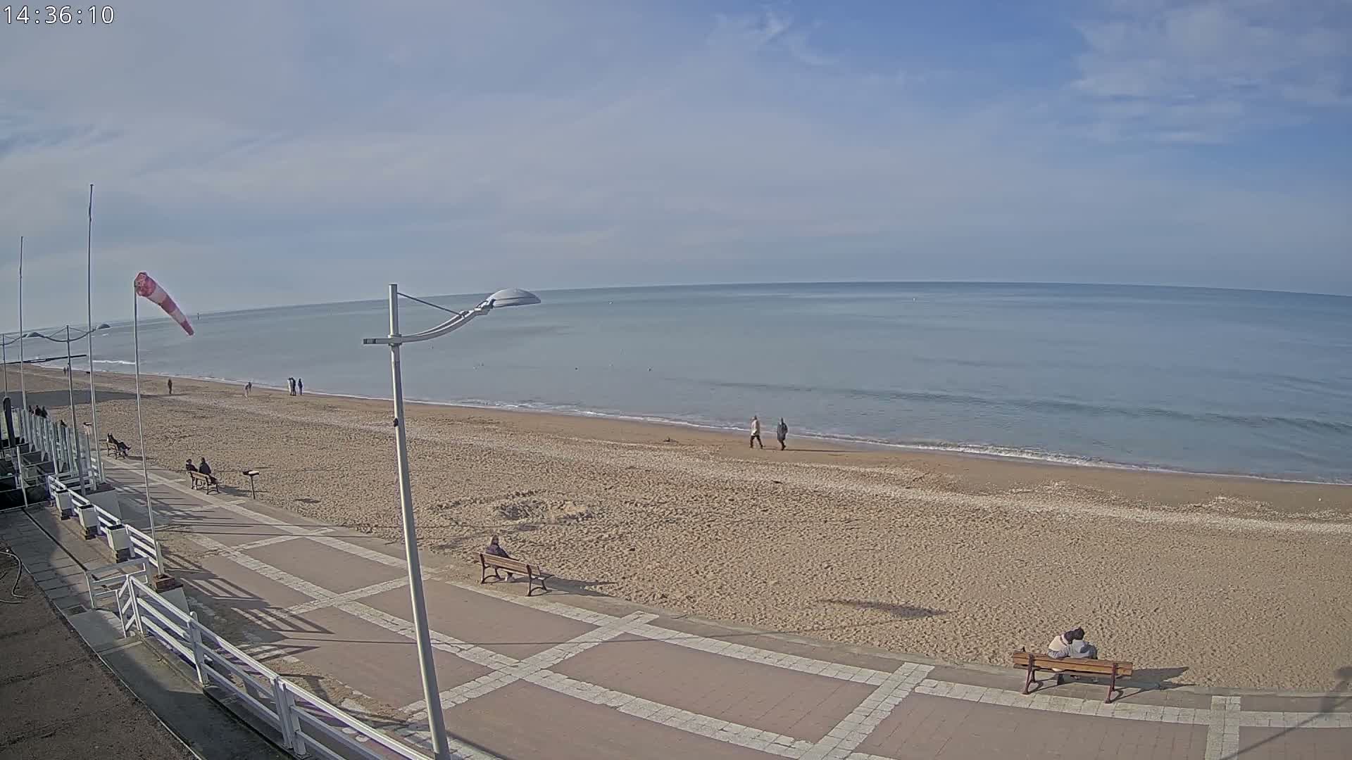 A mostly empty sandy beach stretches to a calm, light-blue ocean under a partly cloudy sky.