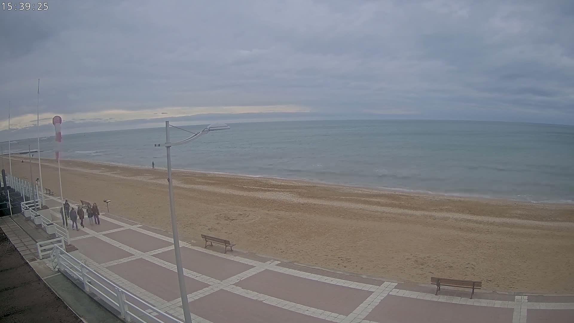 A paved walkway overlooks a sandy beach and calm ocean under a cloudy sky.