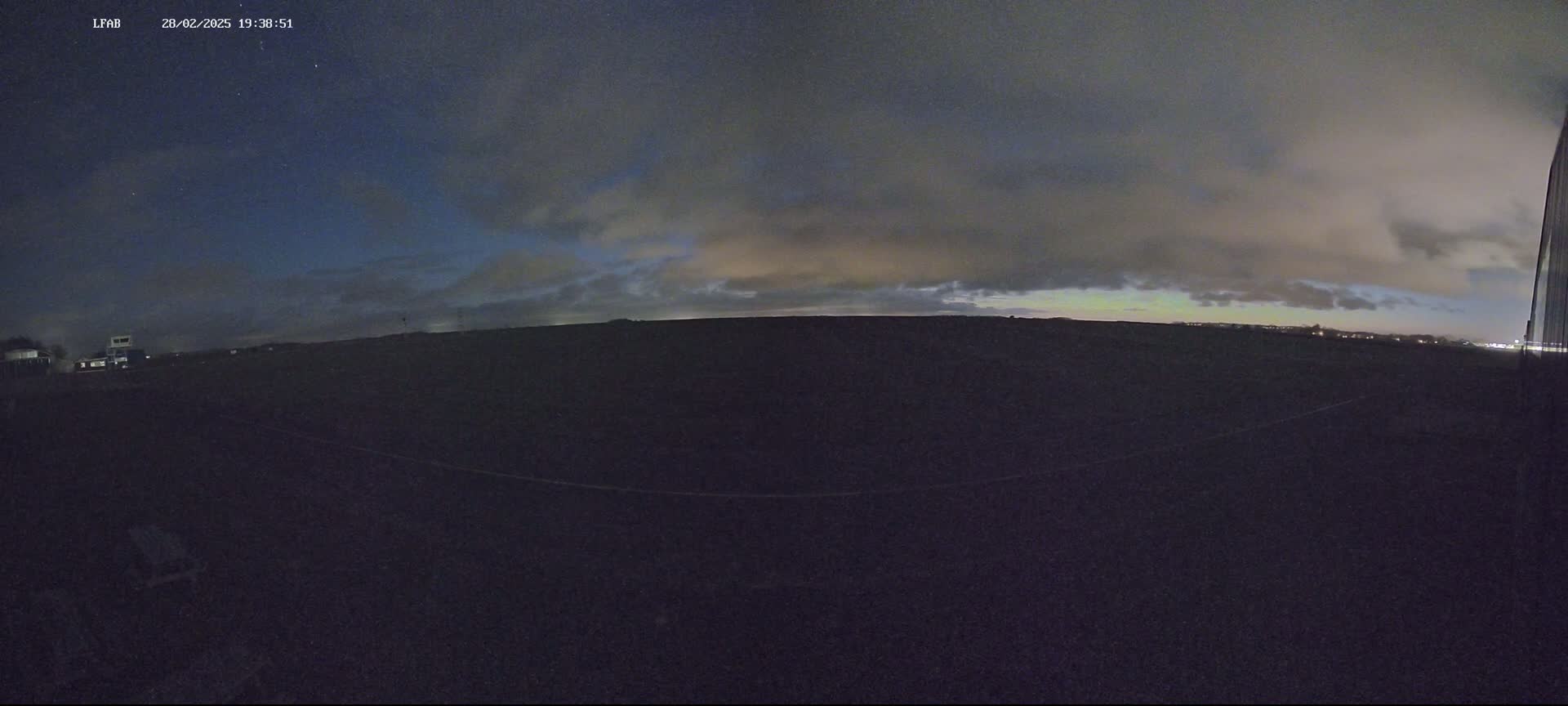 A dark, flat landscape is visible under a mostly cloudy night sky with a hint of color on the horizon.