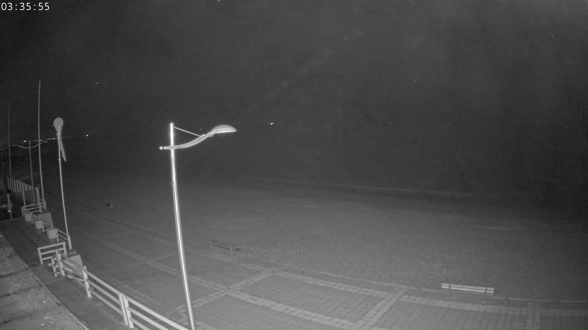 A nighttime, low-light view of an empty beach with lampposts and a railing.