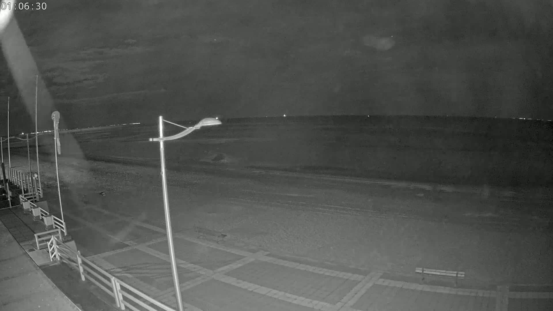 A nighttime view of a mostly empty beach with a calm sea under a dark sky.