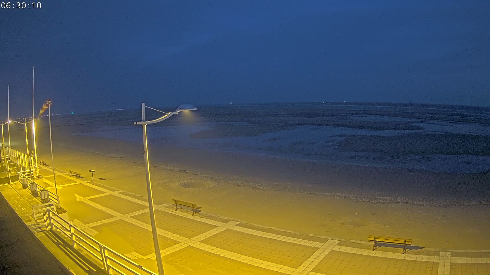 A paved walkway overlooks a dark, sandy beach and calm ocean under a twilight sky.