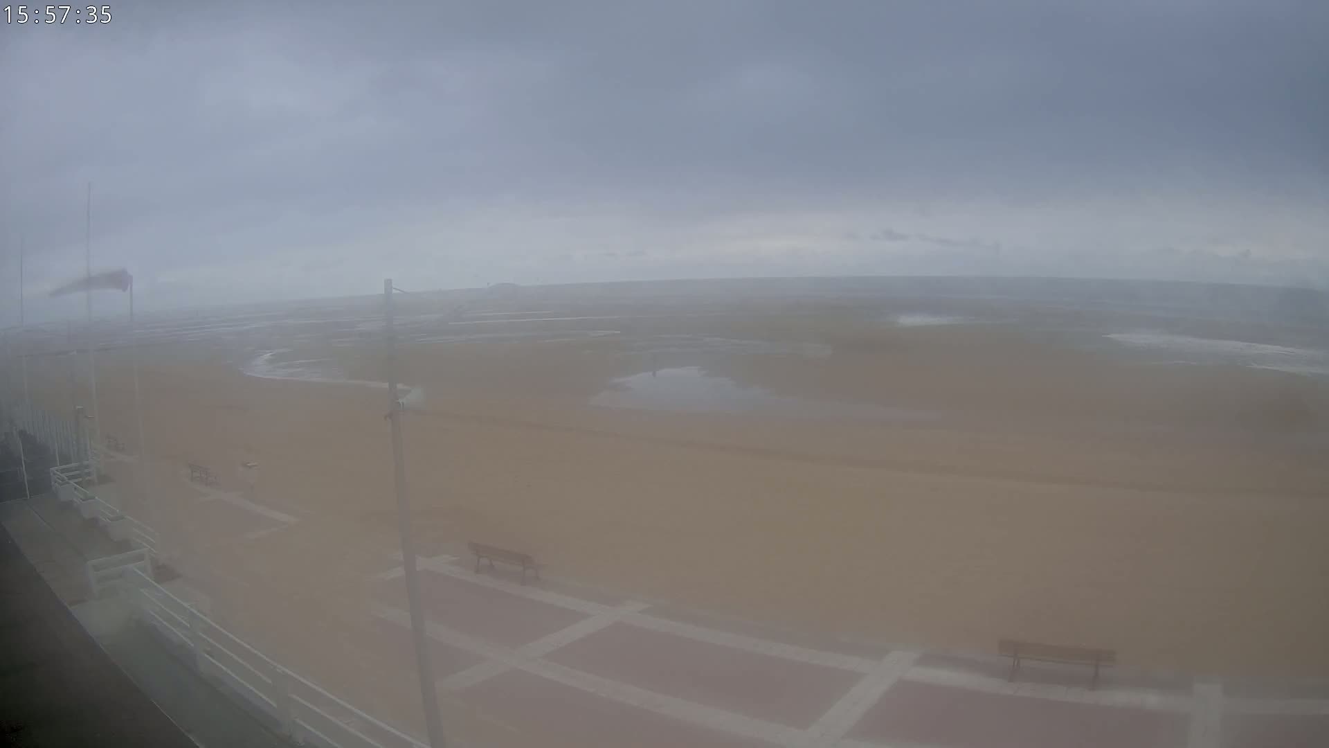 A hazy, overcast day reveals a sandy beach with a promenade, benches, and a distant ocean under a muted sky.
