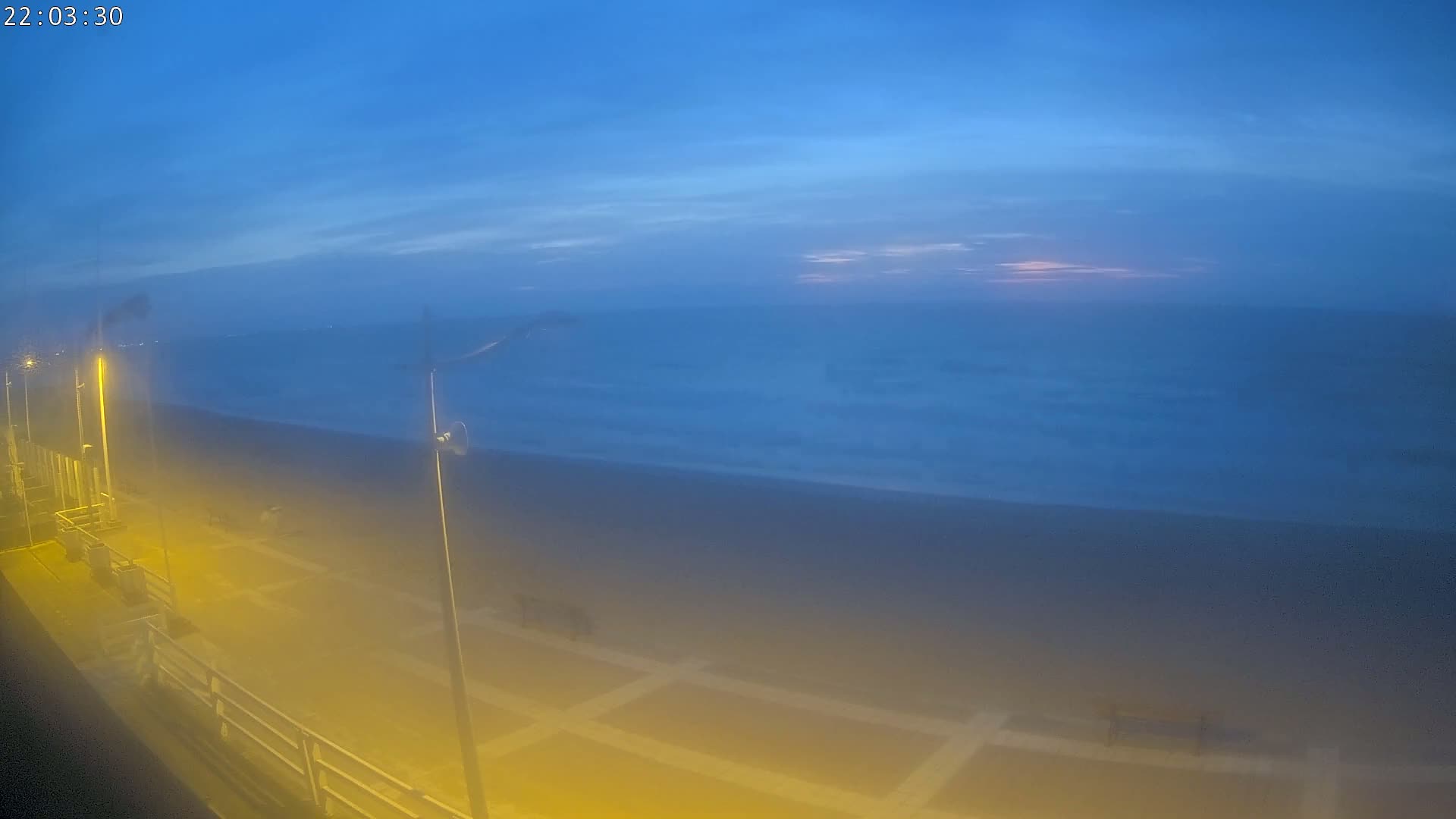 A hazy twilight scene shows a dark beach and ocean under a mostly clear, blue sky.