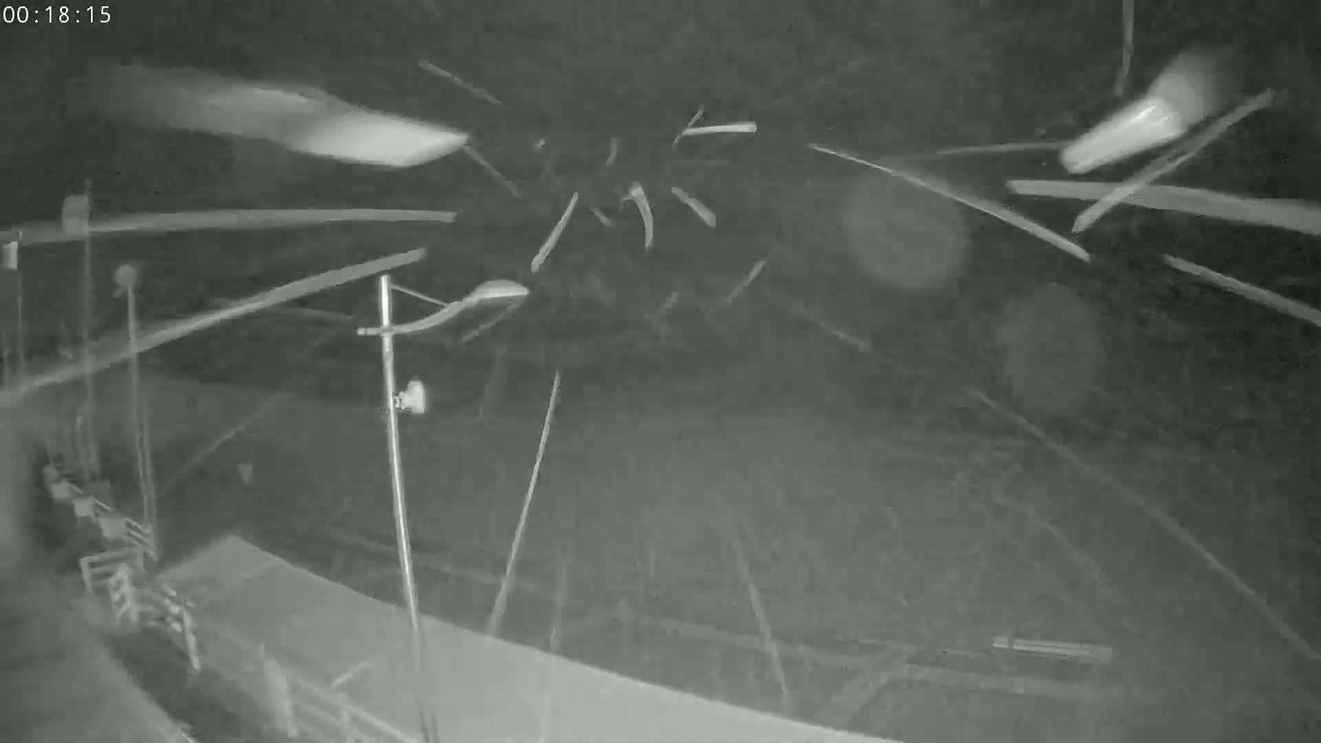 A nighttime outdoor scene shows streaks of falling snow or ice against a dark background, with some indistinct structures and lighting in the lower portion of the frame.