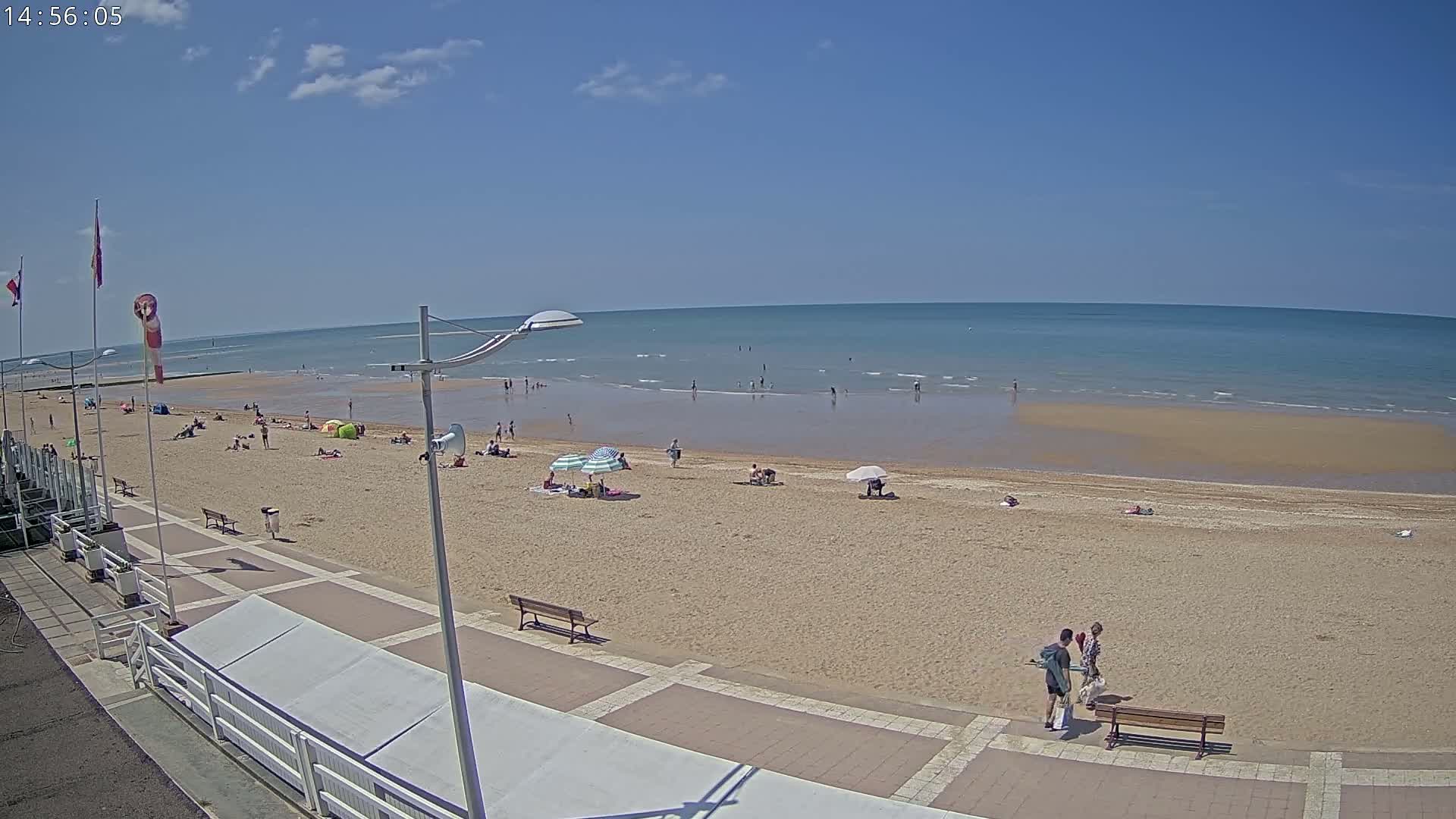A sandy beach with a few people and umbrellas under a clear blue sky.