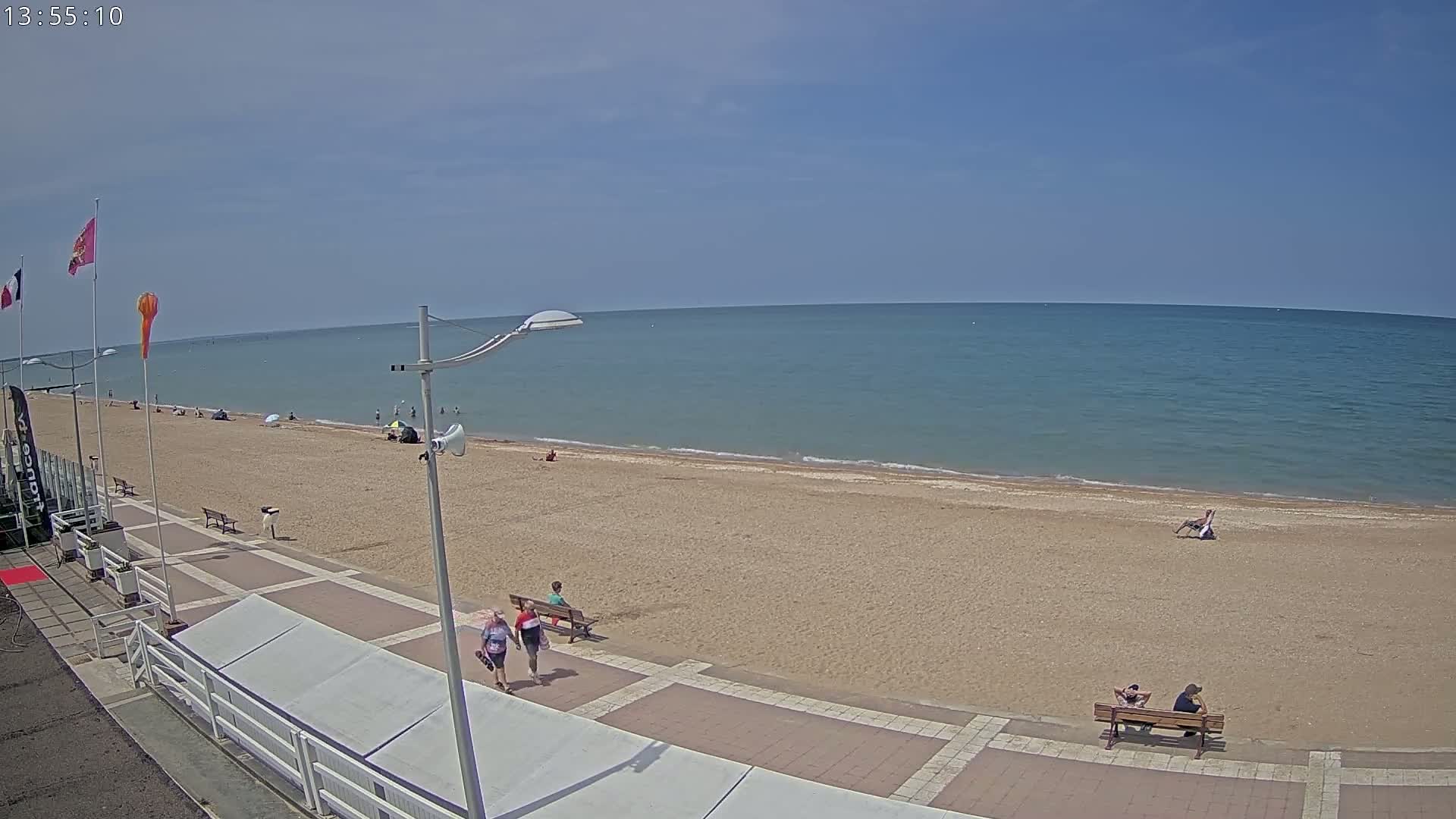 A sandy beach with a few people on it and a calm, blue ocean under a clear sky stretches out to the horizon.