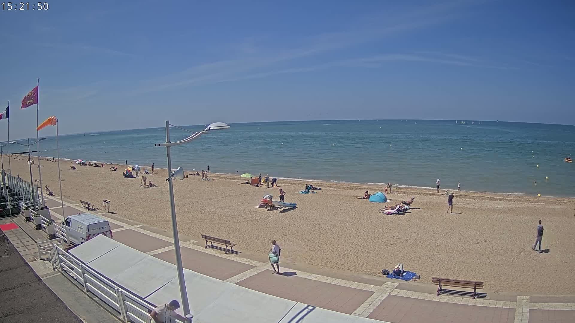 A sandy beach with scattered sunbathers and a calm, blue ocean under a clear, sunny sky.