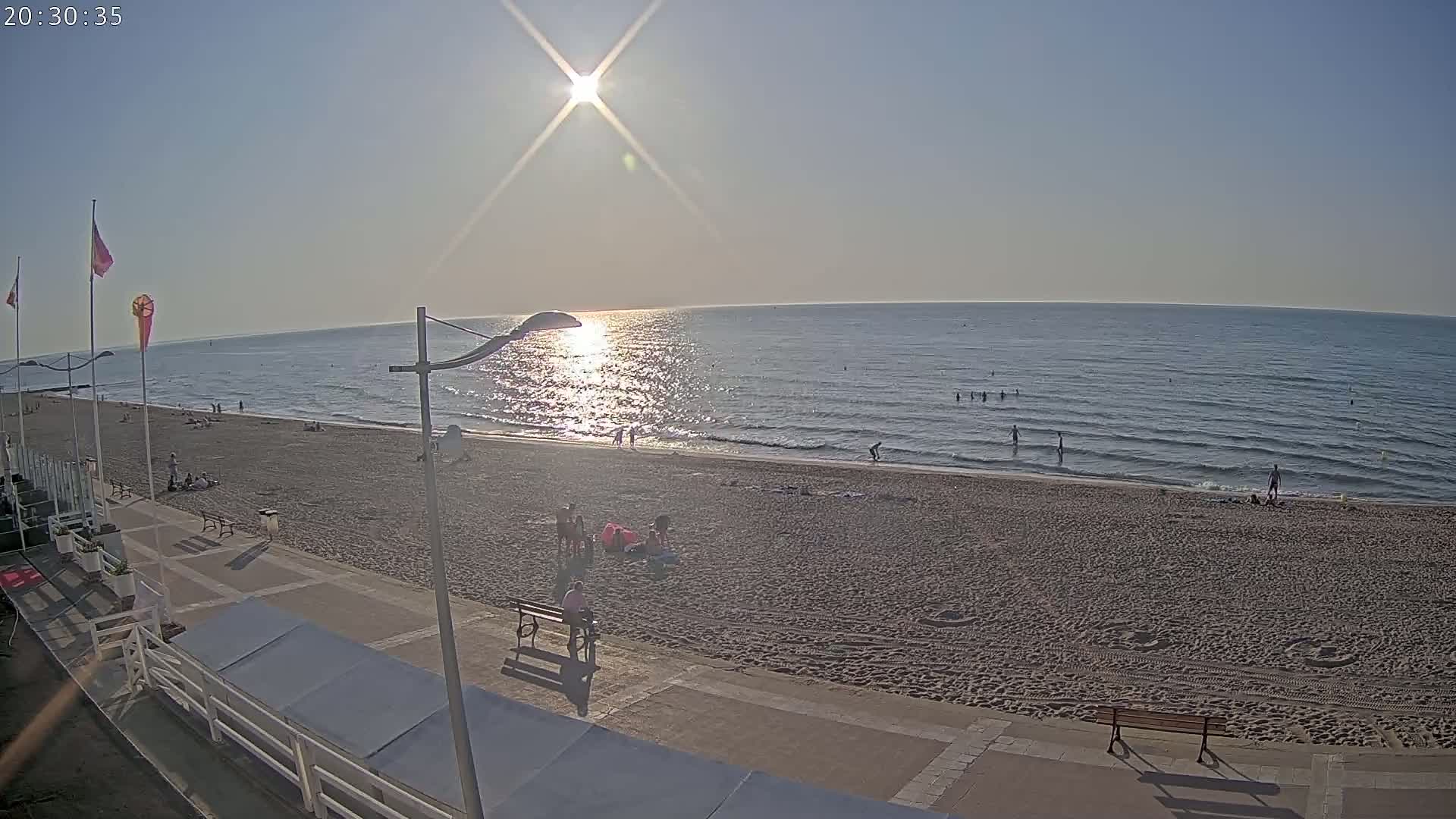 A sandy beach with a few people on it and a calm, sunlit ocean stretches out under a clear sky.