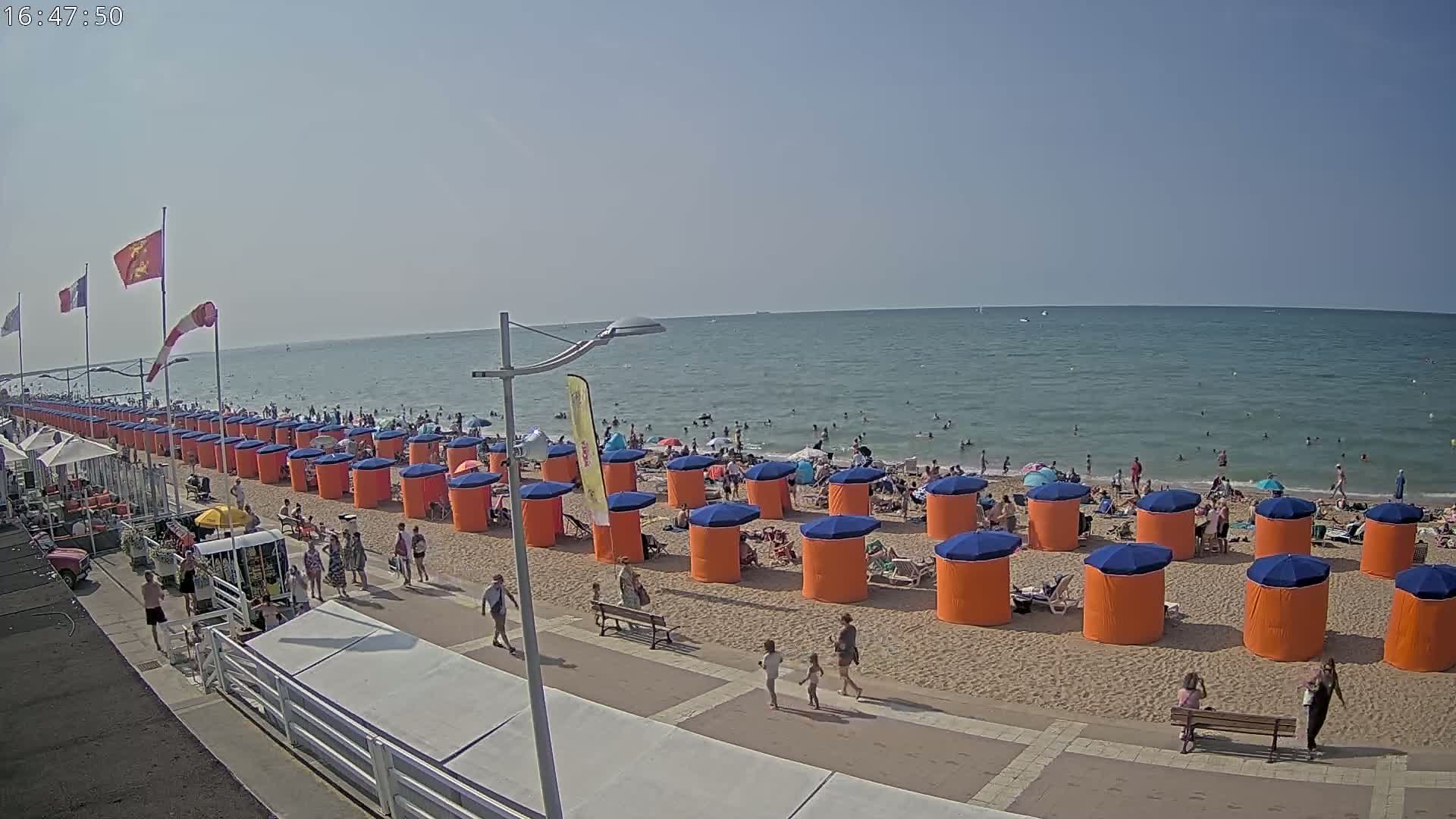 A sandy beach with rows of orange and blue beach cabanas, a boardwalk, and a somewhat choppy grey sea under a cloudy sky.