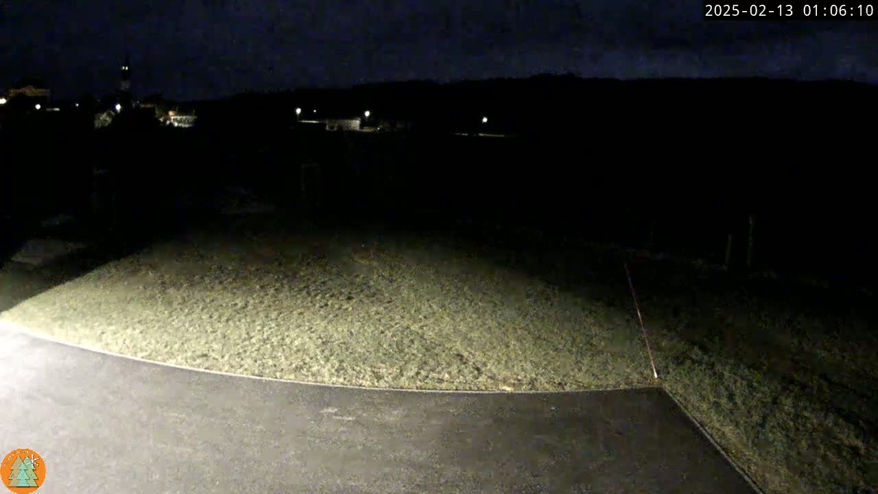A dark, nighttime scene shows a grassy hill illuminated by a light source, sloping down to a paved area.