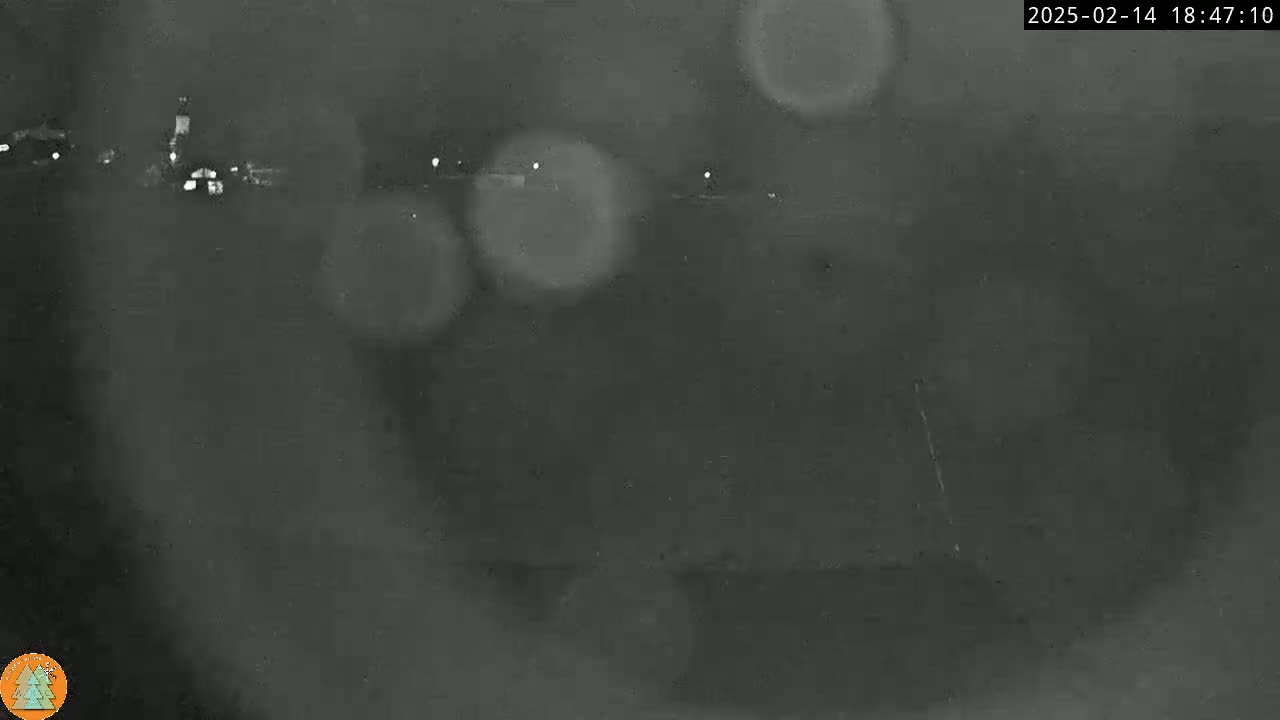 A blurry, nighttime image shows a distant, dimly lit landscape with some lights visible in the background, possibly through rain or fog.