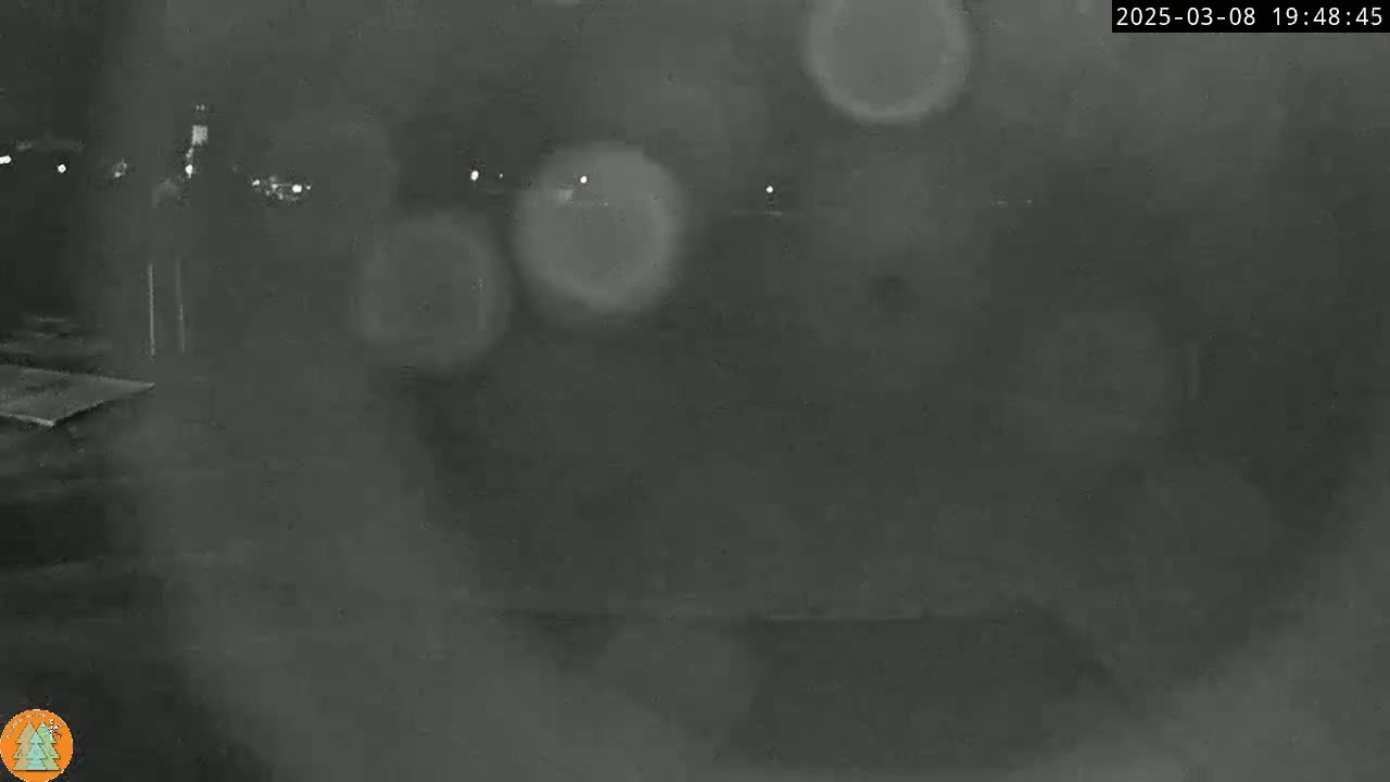 A blurry, dark nighttime scene shows indistinct shapes and out-of-focus lights through what appears to be rain or snow.