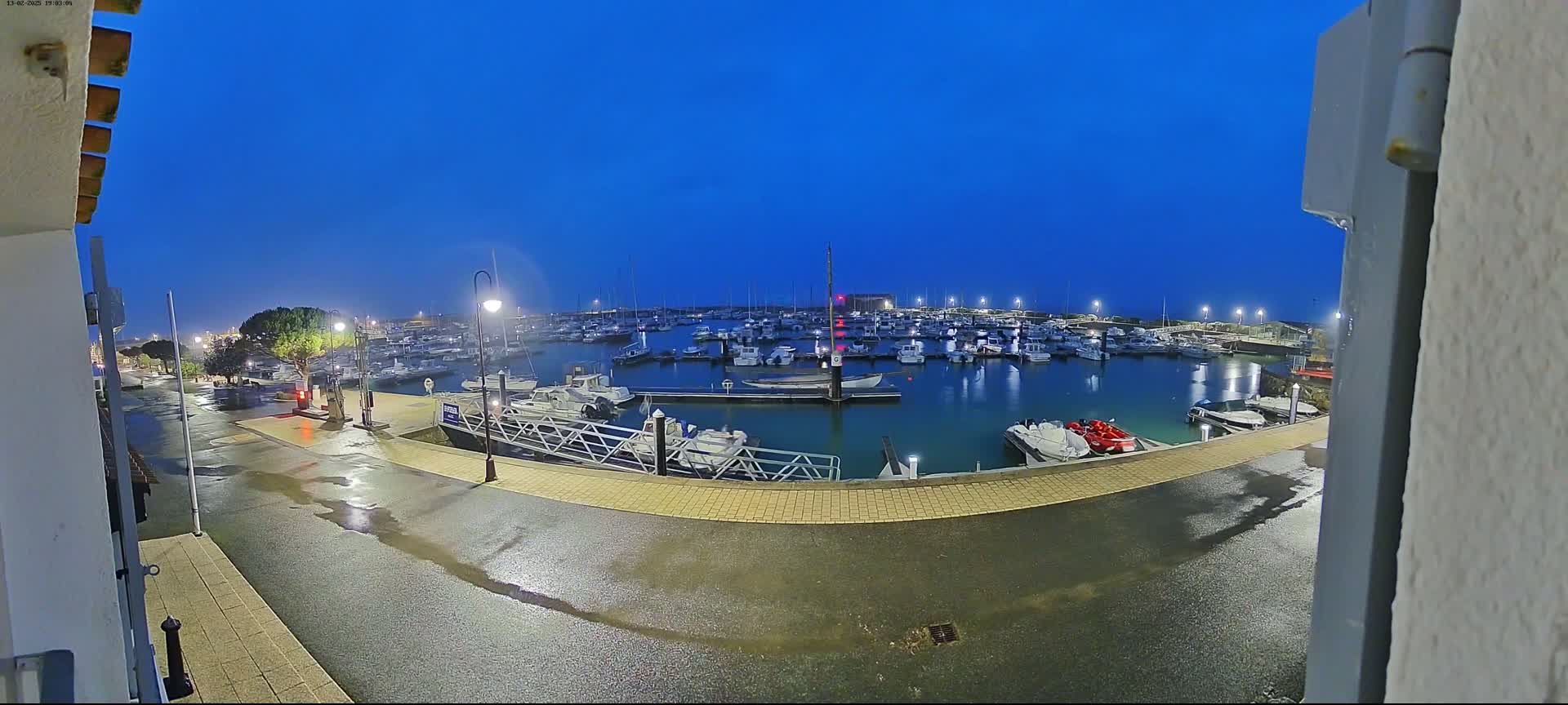 A wet marina at night, under a twilight blue sky, is filled with numerous boats docked along its edges.