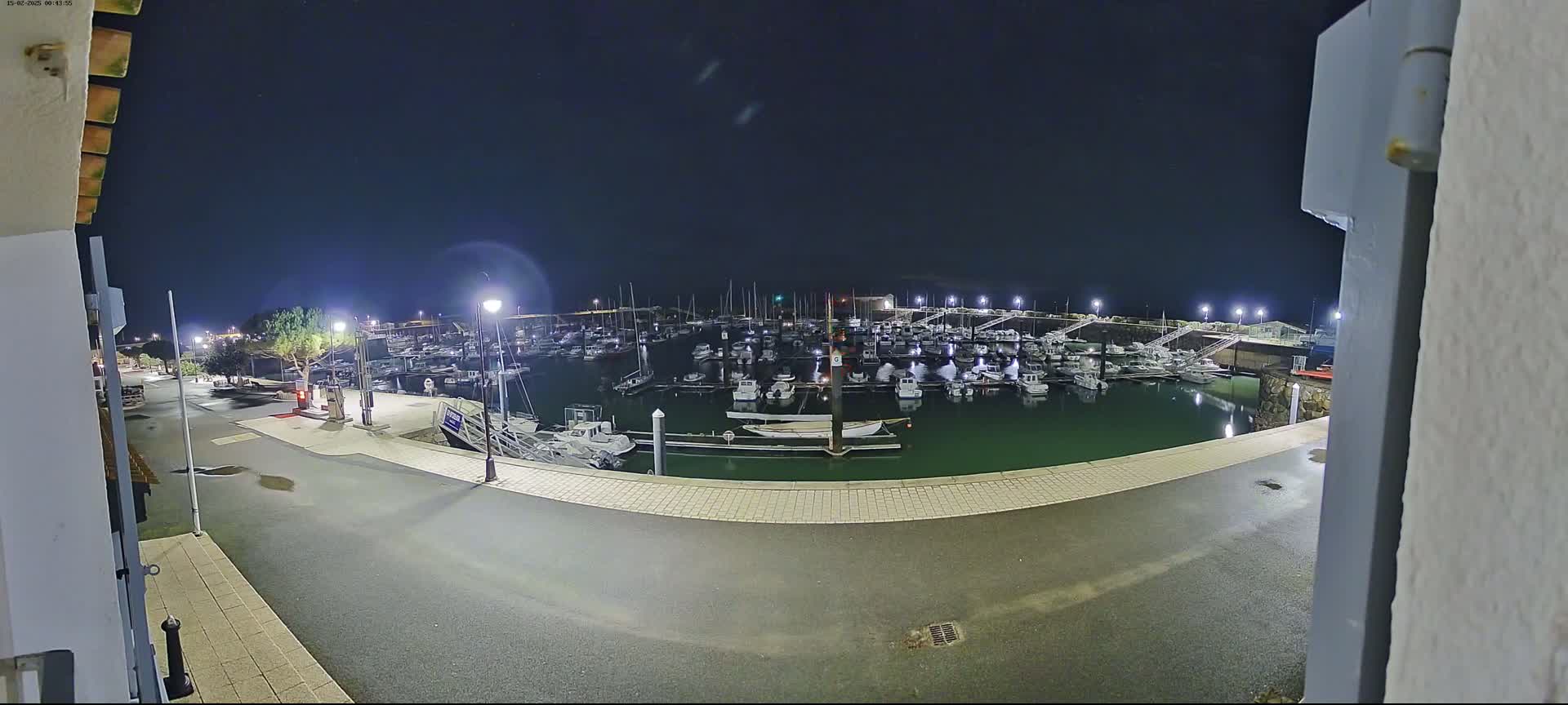 A nighttime view of a harbor filled with numerous boats, illuminated by lights under a clear, dark sky.