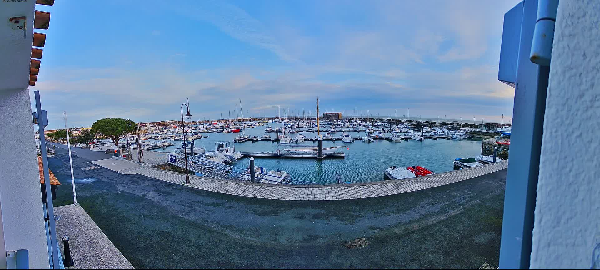 A marina filled with numerous boats is viewed from a slightly elevated position on a mostly clear day.