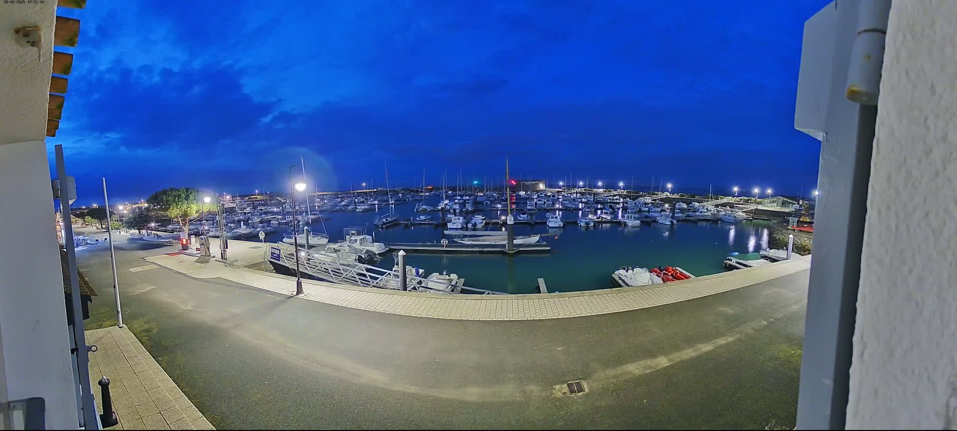 A marina filled with numerous boats is seen at twilight under a mostly clear, dark blue sky.