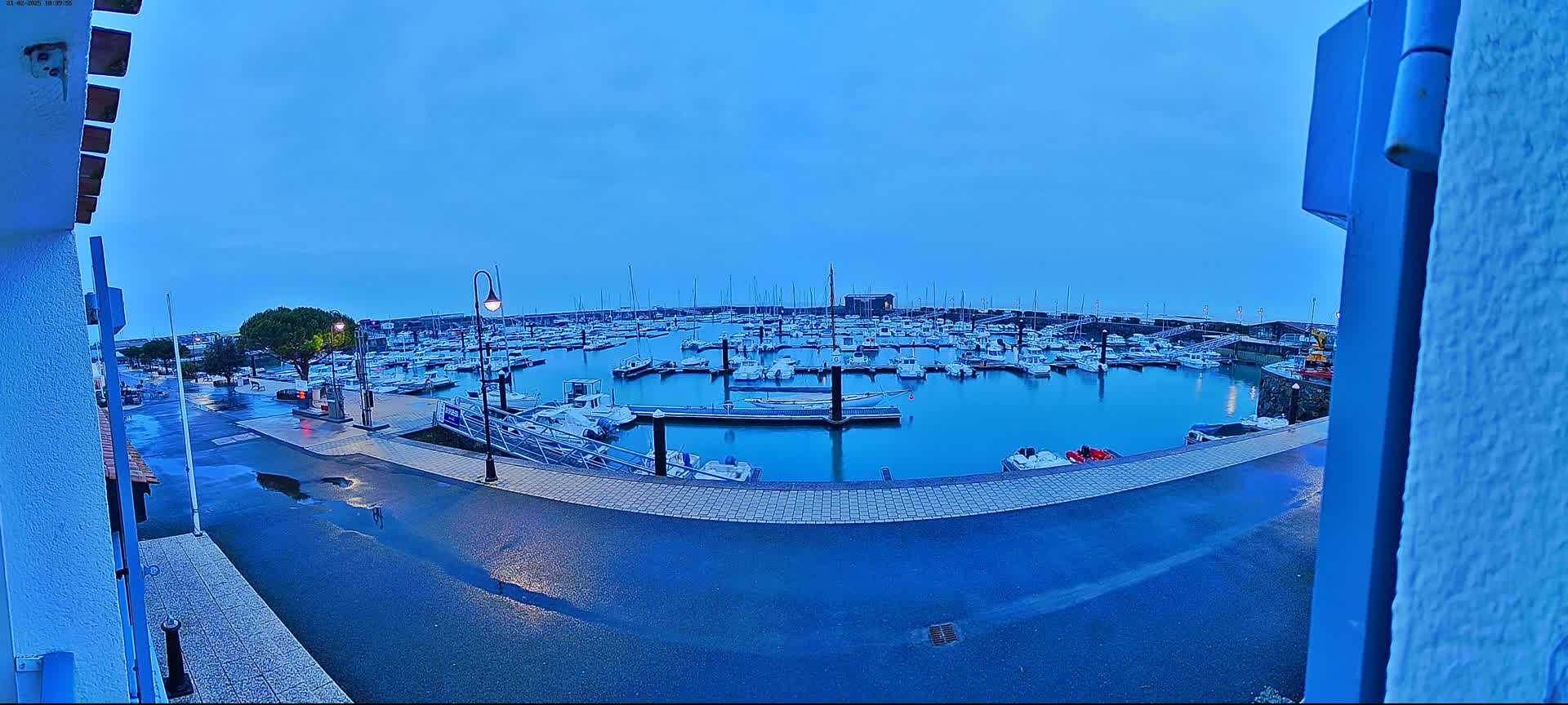 A wet marina filled with many boats is seen at dusk under a clear, blue sky.