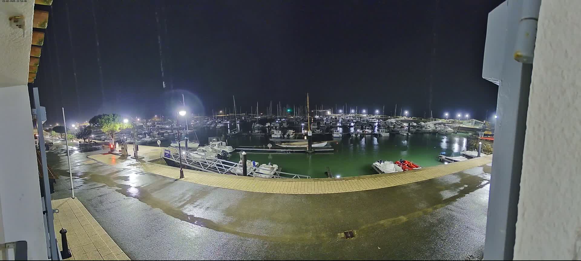A nighttime view of a marina filled with boats under a light rain.