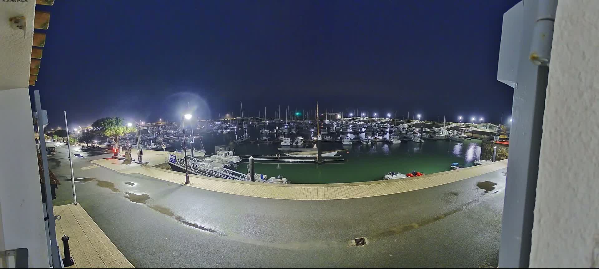 A wet nighttime marina filled with boats is seen from a slightly elevated vantage point.