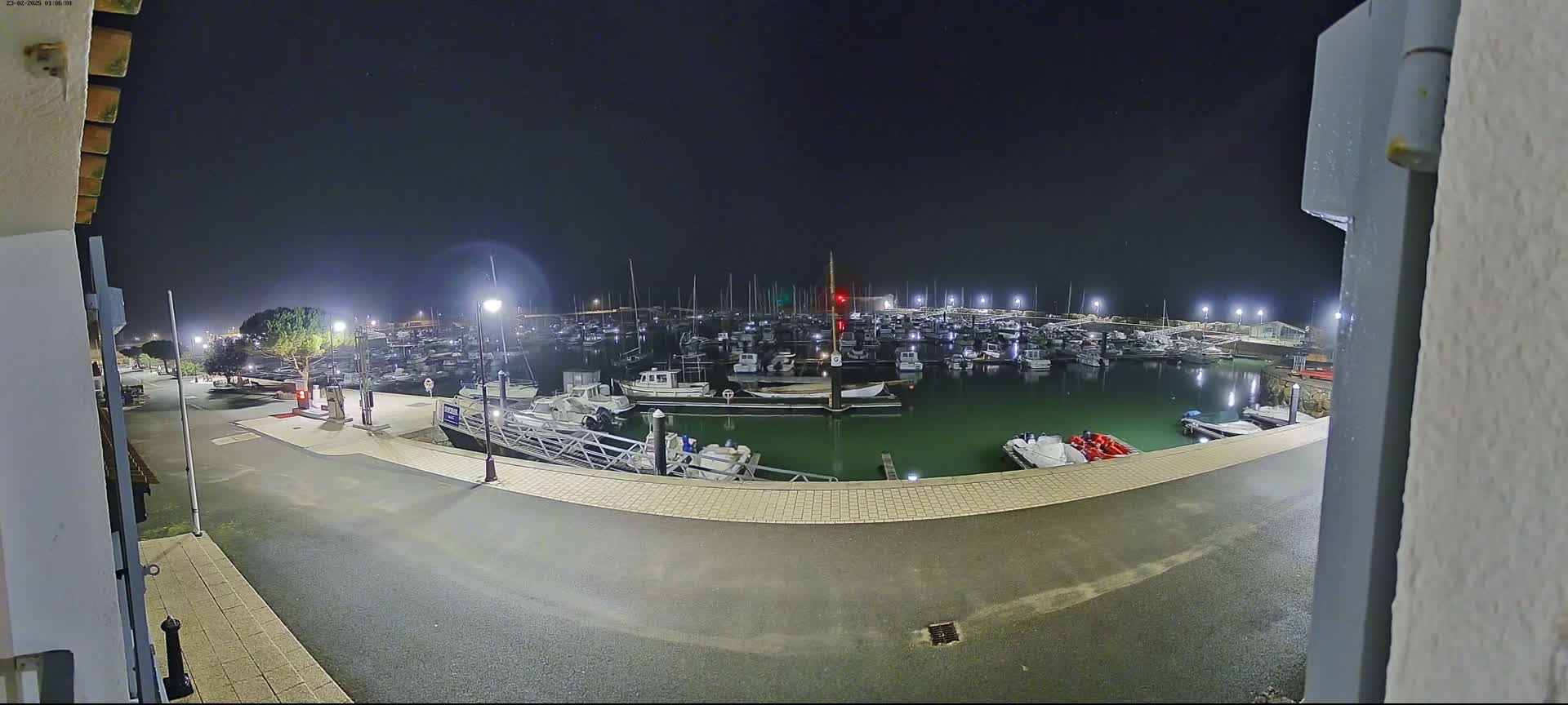 A nighttime view from a building shows a marina filled with numerous boats illuminated by artificial lights under a clear, dark sky.