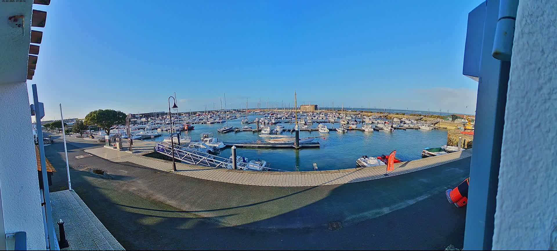 A marina filled with numerous boats on a sunny day is viewed from a slightly elevated position.
