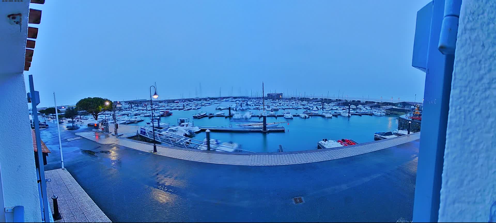 A wet, overcast harbor filled with numerous boats is viewed from a waterfront building.
