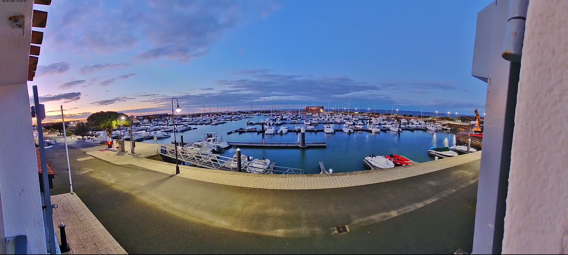 A marina filled with numerous boats is seen at dusk under a partly cloudy sky.