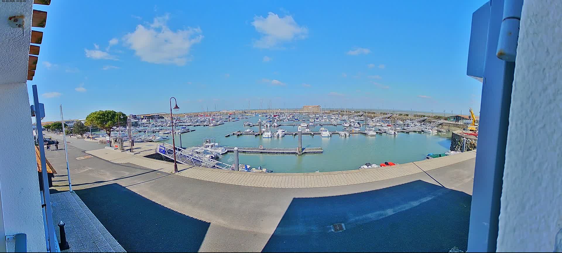 A marina filled with numerous boats is visible under a mostly sunny sky with a few scattered clouds.