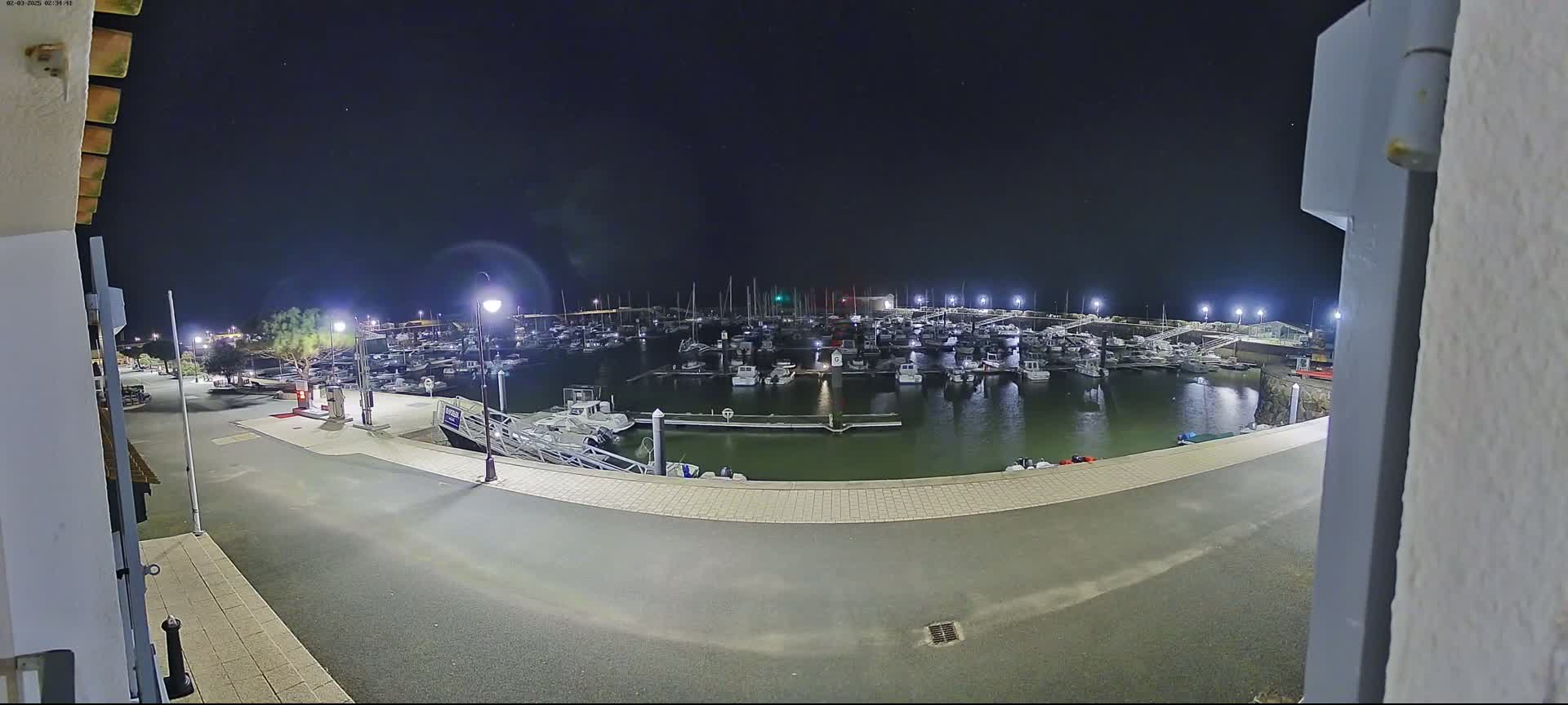A nighttime view of a marina filled with boats, illuminated by artificial lights under a clear, dark sky.