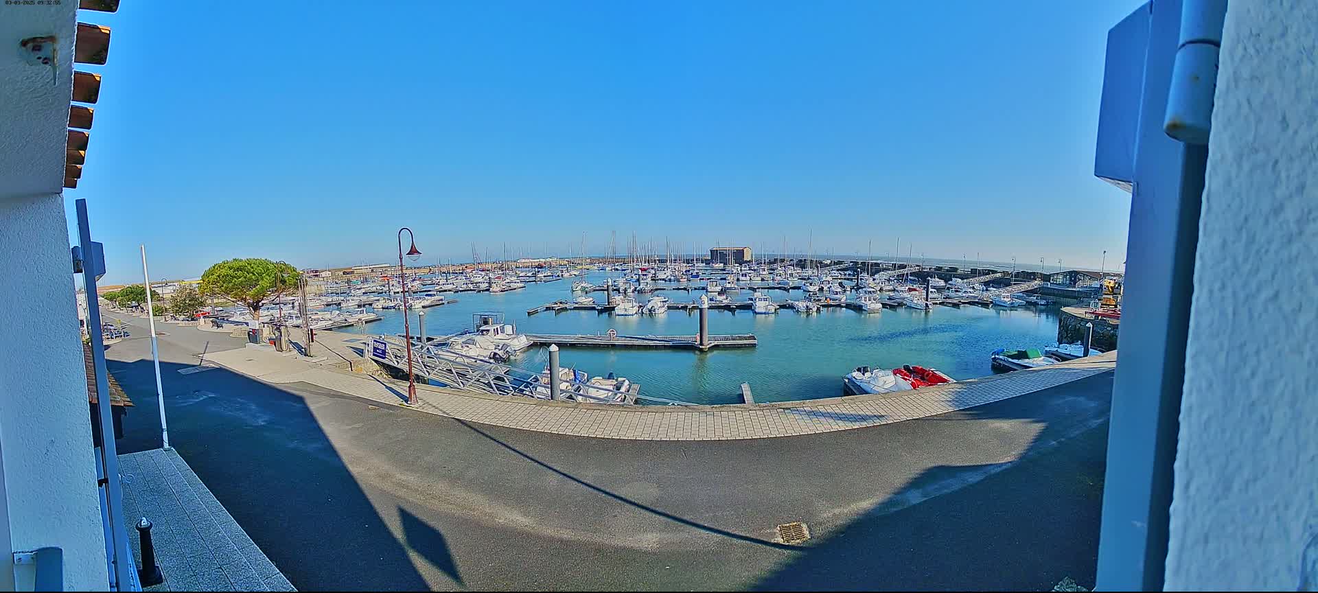 A marina filled with numerous boats is visible on a sunny day, seen from a slightly elevated viewpoint.