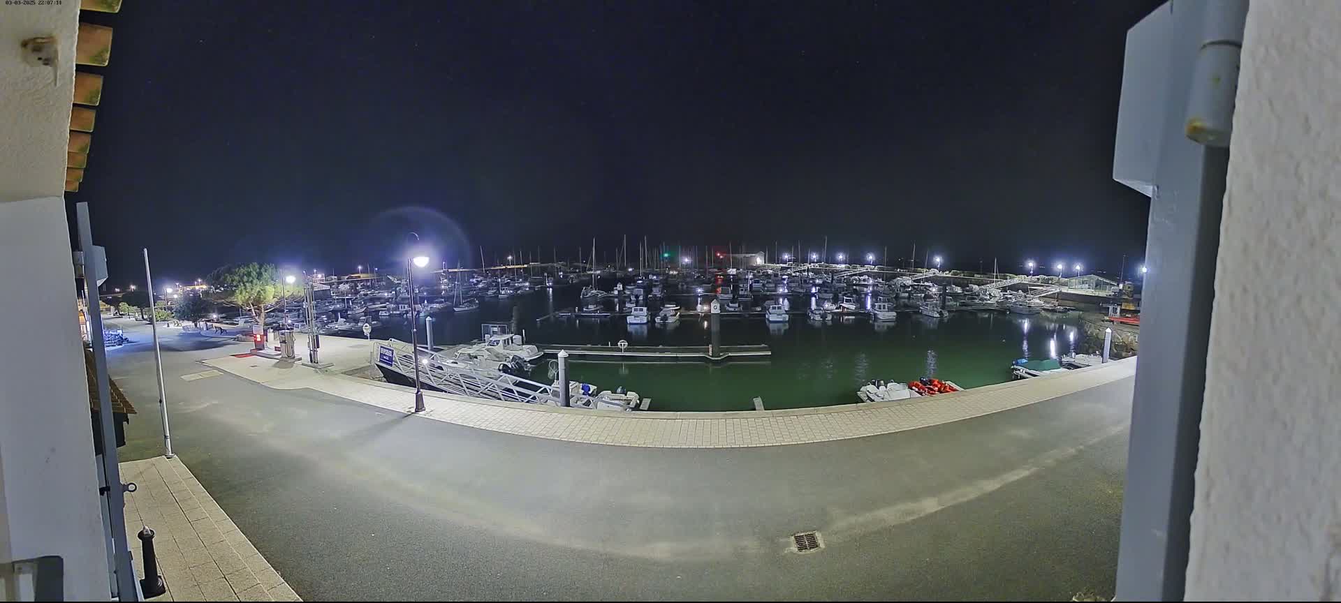 A nighttime view of a marina filled with boats, illuminated by lights under a clear, starry sky.