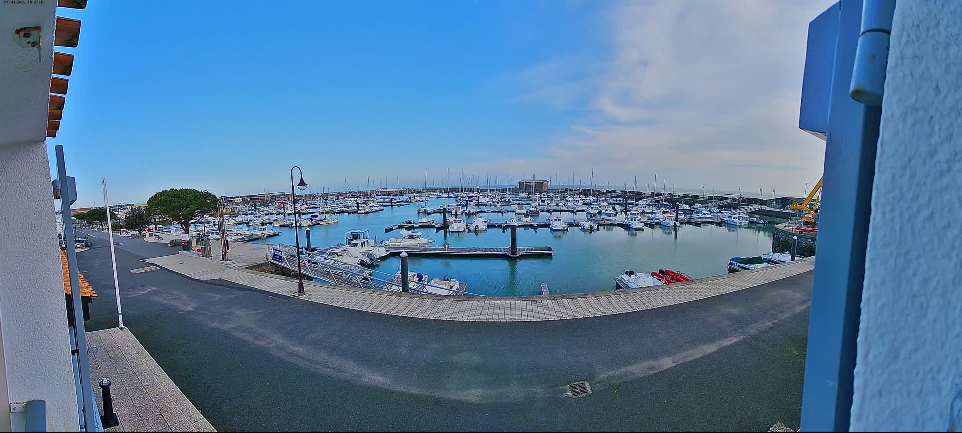 A marina filled with numerous boats is viewed from a slightly elevated position on a mostly sunny day.