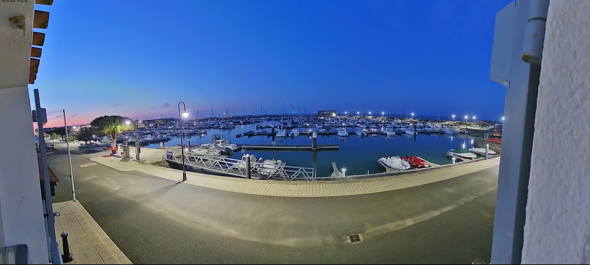 A marina filled with numerous boats is seen at dusk under a clear blue sky.