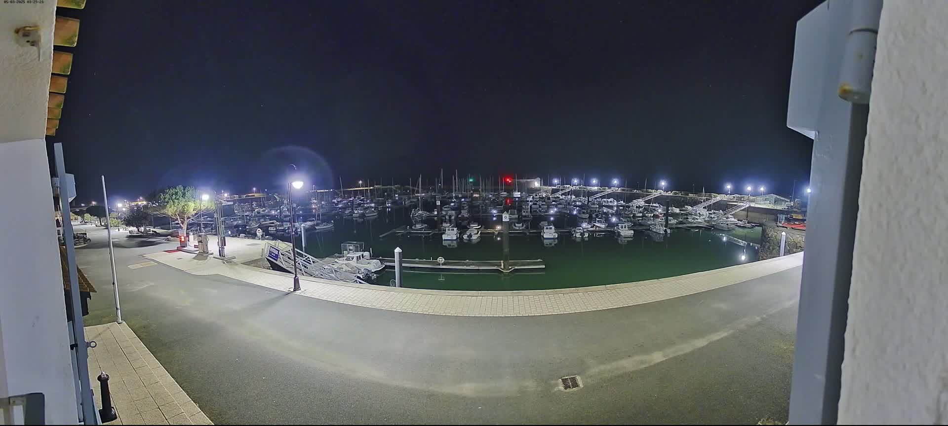 A nighttime view of a marina filled with numerous boats, illuminated by artificial lights under a clear, dark sky.