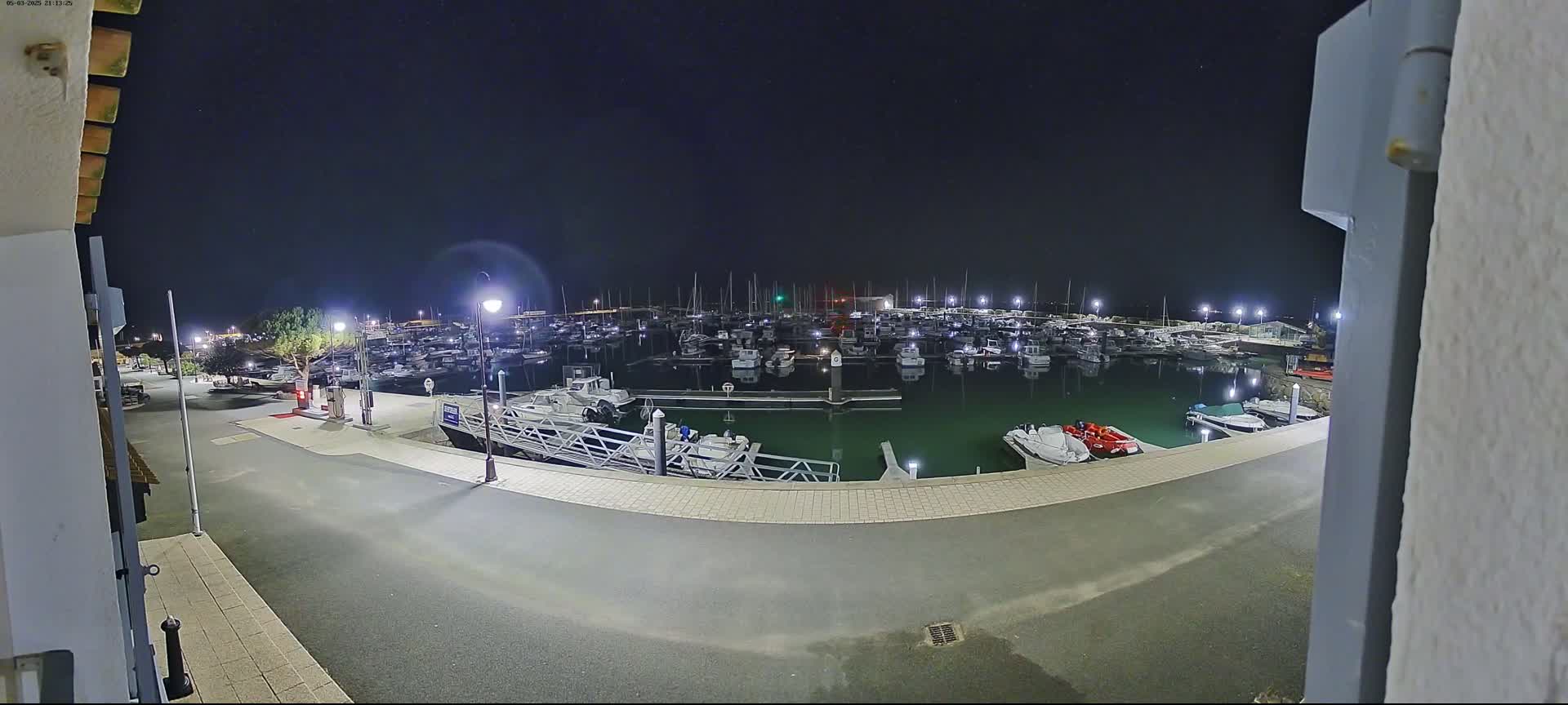 A nighttime view of a marina filled with numerous boats, illuminated by lights under a clear, dark sky.